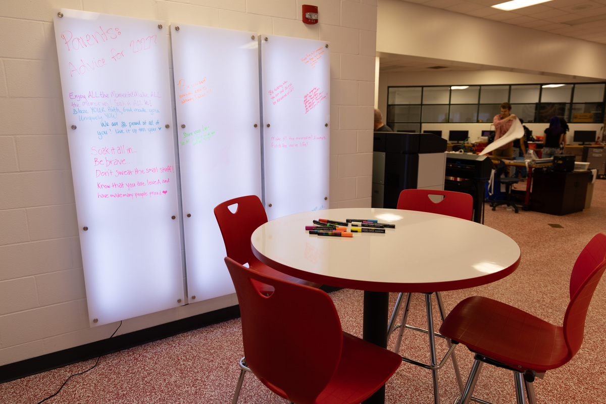 A hightop table and red chairs in front of back lit white boards with writing in the Innovation Lab at MLSD.